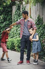 Mixed race brothers and sister playing on suburban sidewalk