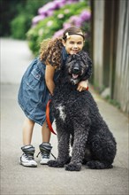 Mixed race girl hugging dog on suburban sidewalk