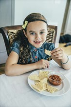 Mixed race girl eating chips and salsa at table