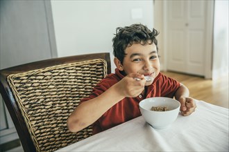 Mixed race boy eating cereal at table
