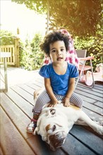 Mixed race girl sitting on dog on porch
