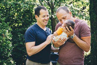 Caucasian gay couple kissing baby boy outdoors