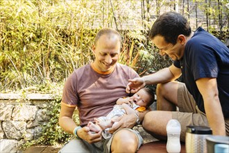 Caucasian gay couple admiring baby boy in backyard