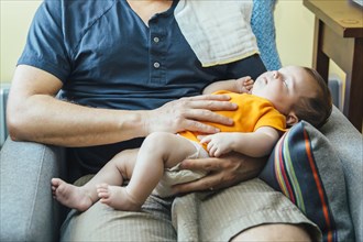 Caucasian father holding sleeping baby boy in armchair
