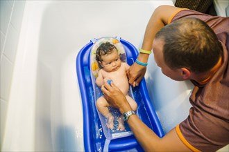 Caucasian father bathing baby boy in bathtub