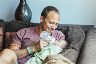 Caucasian father feeding baby boy on sofa