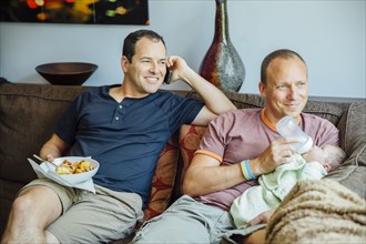 Caucasian gay couple relaxing with baby boy on sofa