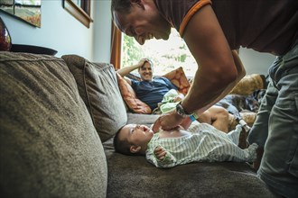 Caucasian father dressing baby boy on sofa