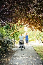 Caucasian gay couple jogging with stroller on sidewalk