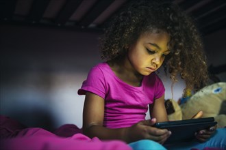 Mixed race girl using digital tablet on bed