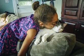 Mixed race girl kissing pet cat on sofa
