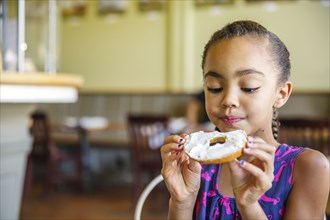 Mixed race girl eating bagel in cafe