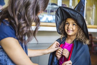 Mother dressing daughter in witch costume