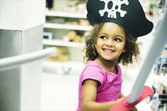 Mixed race girl playing dress-up with pirate hat and sword