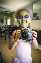 Mixed race girl in face paint photographing with camera
