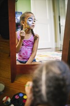 Mixed race girl painting her face in bedroom