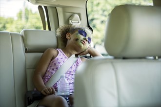 Mixed race girl in face paint sleeping in car back seat