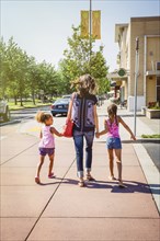 Mother and daughters holding hands on neighborhood sidewalk