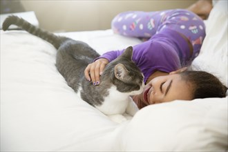 Mixed race girl playing with cat on bed