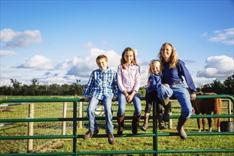 Caucasian farmer and children sitting on fence on ranch