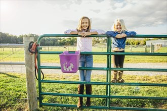 Caucasian girls standing on fence on ranch