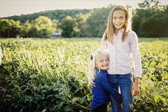 Caucasian sisters hugging in crop field on farm