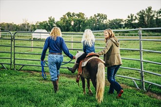Three generations of Caucasian women walking miniature horse on farm