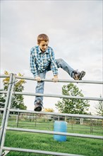 Caucasian boy climbing fence on farm