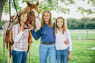 Three generations of Caucasian women standing near horse on farm