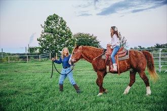 Caucasian mother and daughter walking horse on ranch
