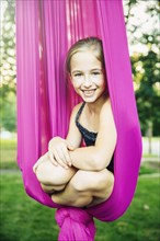 Acrobatic Caucasian girl sitting in hanging fabric