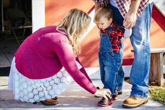 Caucasian mother tying shoes of son outside barn