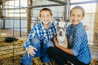 Caucasian brother and sister petting goat in barn