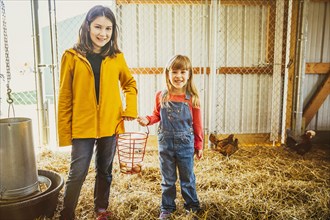 Caucasian sisters collecting chicken eggs in barn