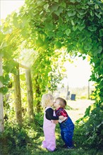 Caucasian children kissing under ivy leaves