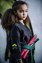 Mixed race girl wearing martial arts uniform with nunchucks