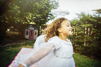 Mixed race girl wearing angel costume in backyard