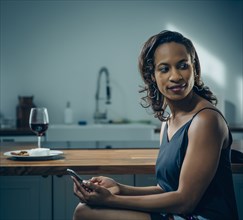 Black woman using cell phone at kitchen counter