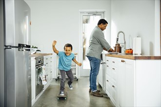 Boy skateboarding near father in kitchen
