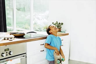 Mixed race boy with skateboard laughing in kitchen