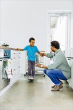Father helping son balance on skateboard in kitchen