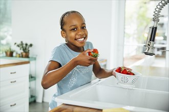Black girl eating strawberries in kitchen