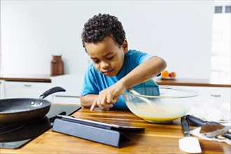 Mixed race boy cooking breakfast with digital tablet in kitchen