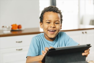 Mixed race boy using digital tablet in kitchen