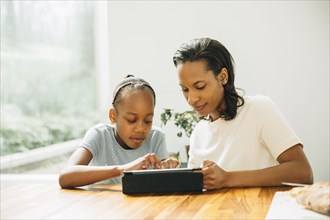 Black mother and daughter using digital tablet at table