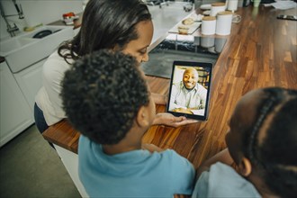 Mother and children video chatting with father in kitchen