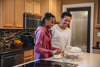 Black mother and daughter decorating cake in kitchen