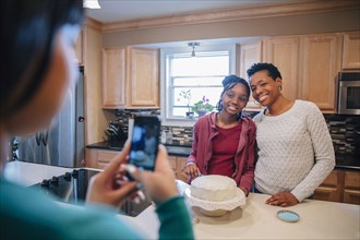 Black woman photographing sister and mother in kitchen