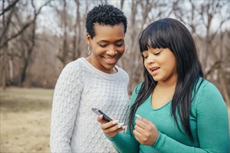 Black mother and daughter using cell phone outdoors