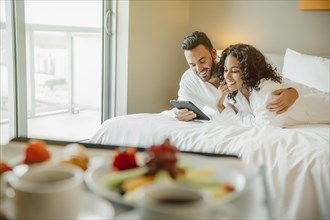 Couple using digital tablet on hotel bed